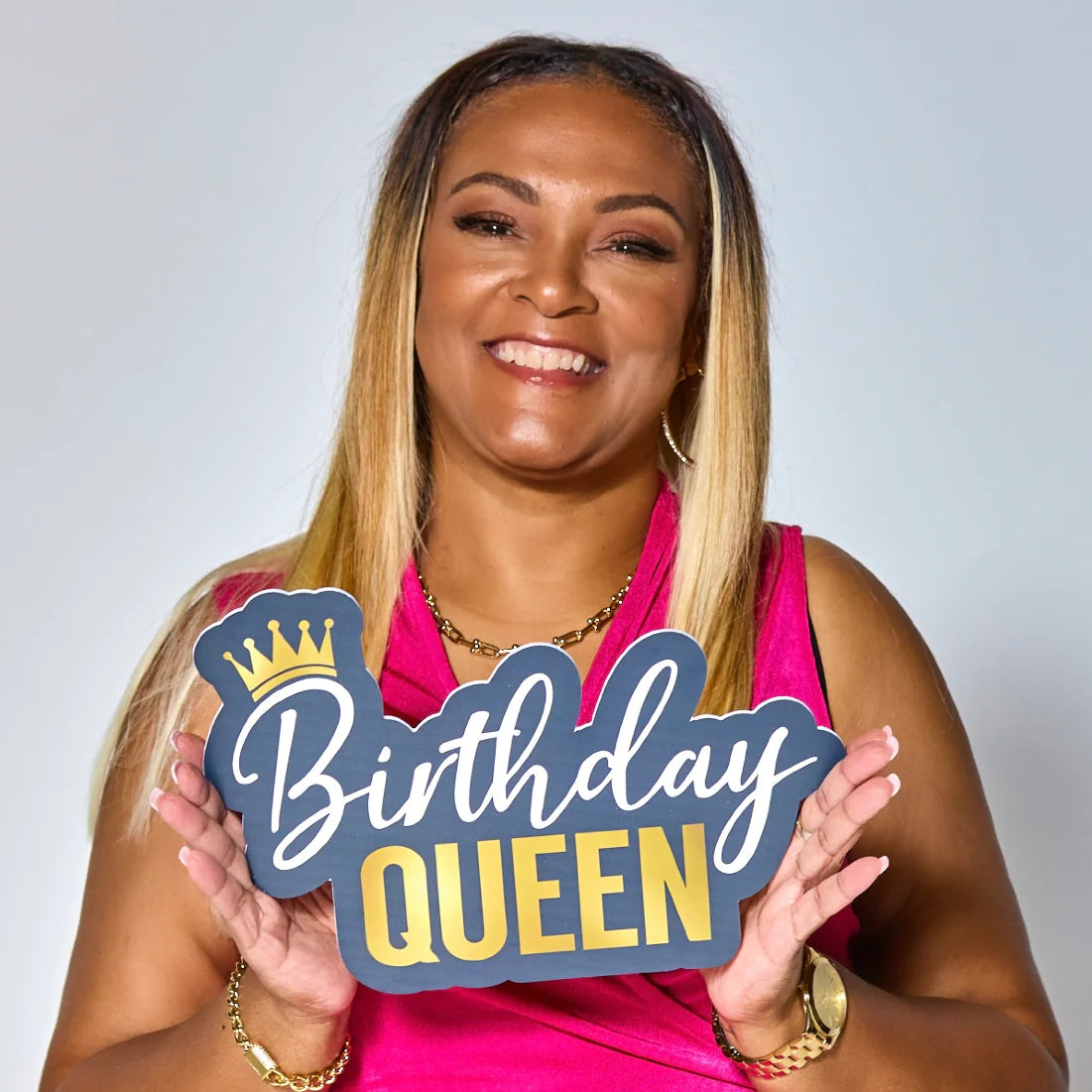 Woman holding a 'Birthday Queen' sign against a plain background