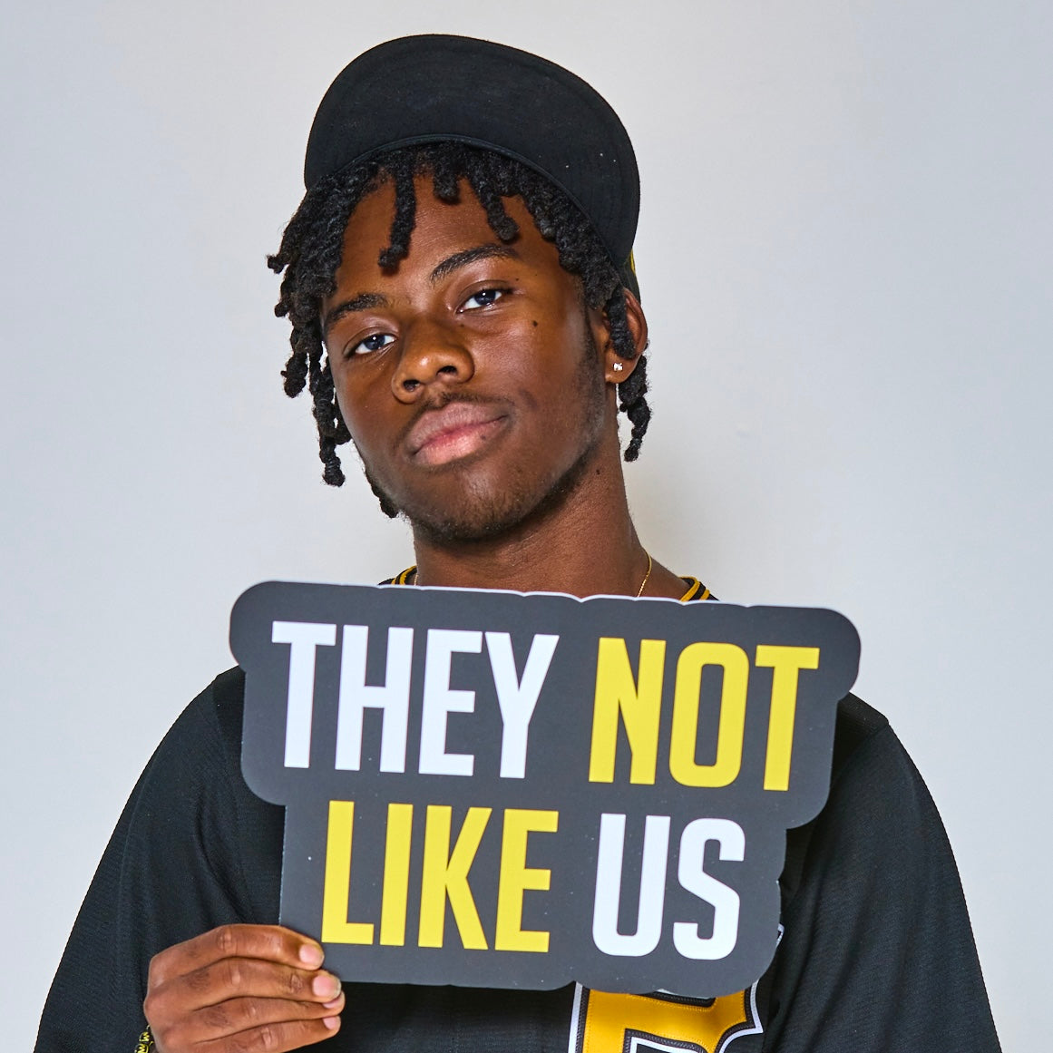 Man holding a black and yellow “They Not Like Us” photo booth prop sign.