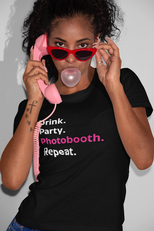 Black unisex t-shirt with bold white and pink text that reads "Drink. Party. Photobooth. Repeat."